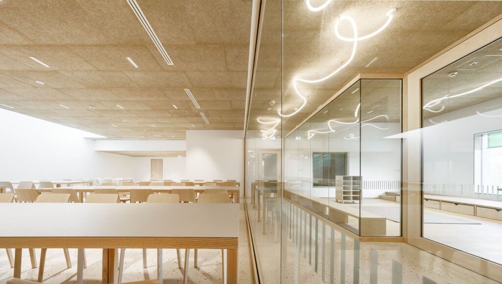 Modern learning area in Barbiano featuring wavy neon ceiling lights, glass partitions, and long wooden tables.