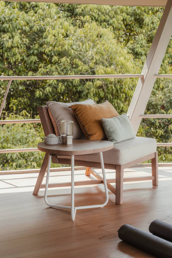 Close-up of a lounge chair and side table on the balcony of Ojo de Nila house against a backdrop of green trees.