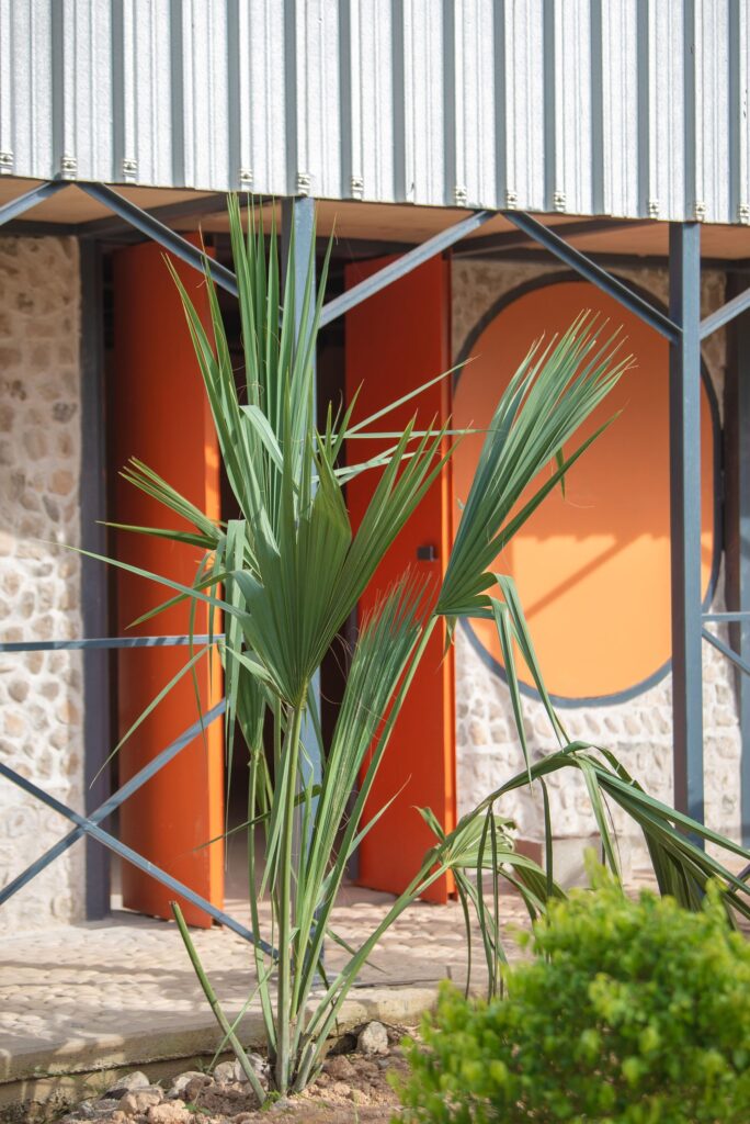 Close-up of the continuous veranda and orange circular doors, showing the integration of tropical plants in the foreground.