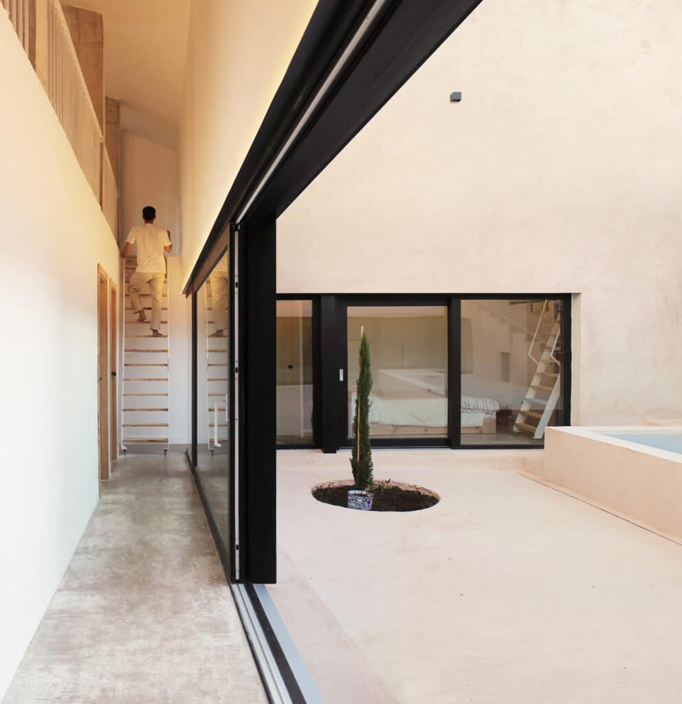 Interior corridor with large glass walls facing the courtyard and a retractable wooden ladder leading to a loft.