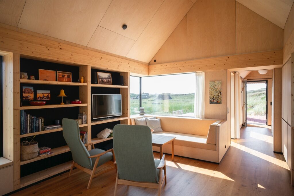 Interior of Kligwood Summer House featuring light wood walls, built-in bookshelves, and a cozy seating area with a view of the dunes.