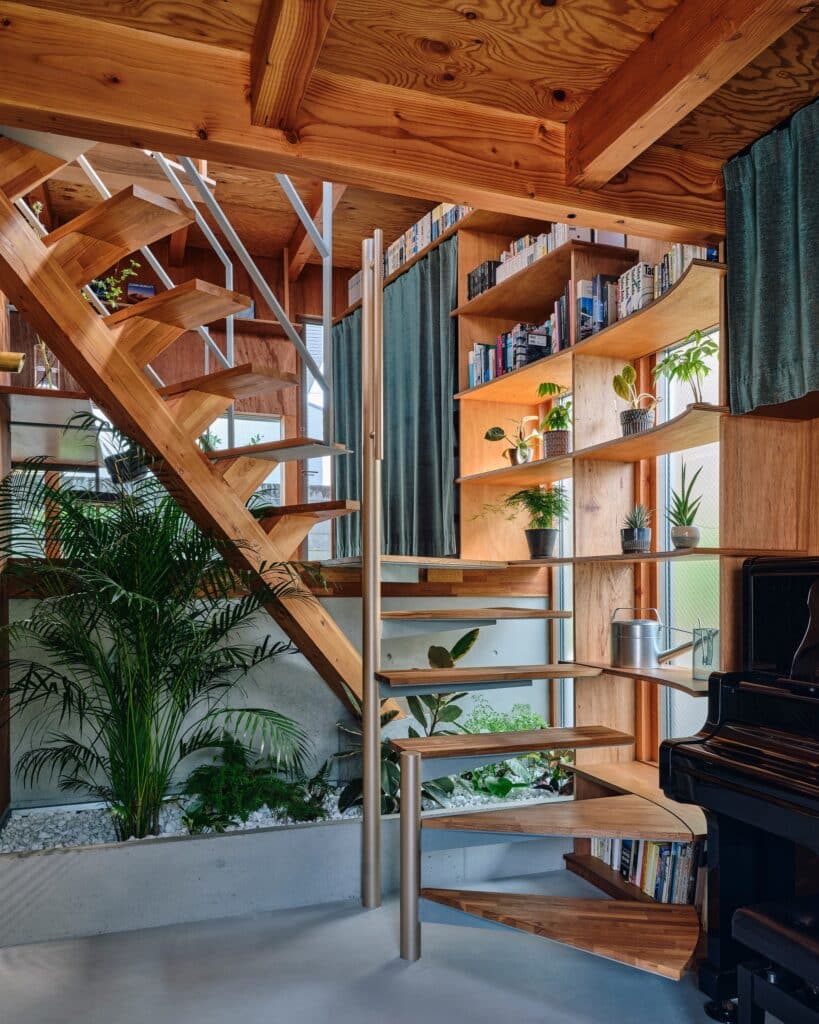 Minimalist wooden stairs next to an indoor plant bed and a piano, showcasing contemporary Japanese interior decoration.