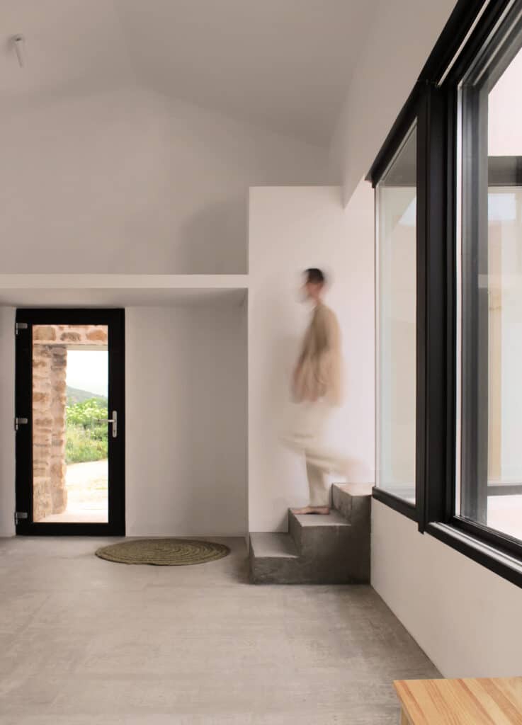 Minimalist interior space with concrete floors, white walls, and a small concrete staircase next to a large window.