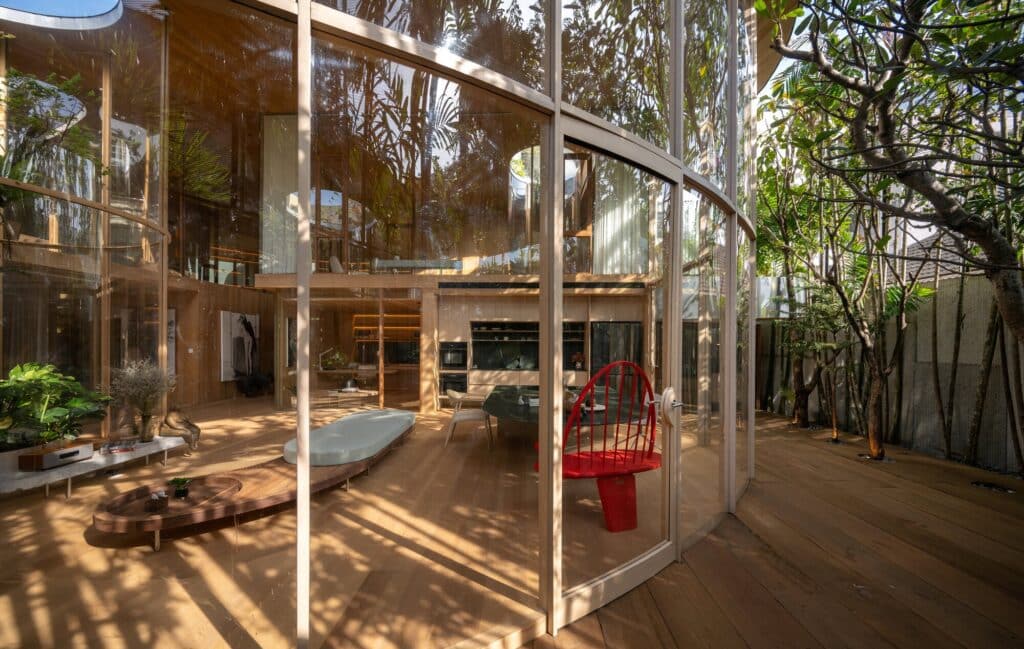 View from the wooden deck toward the glass-enclosed living room of Terrarium House, showing the integration of indoor and outdoor spaces.
