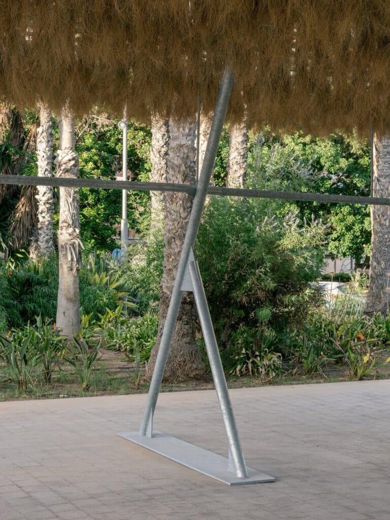 Close-up of the galvanized steel tripod leg supporting the Espartal pavilion's roof structure on a paved surface.
