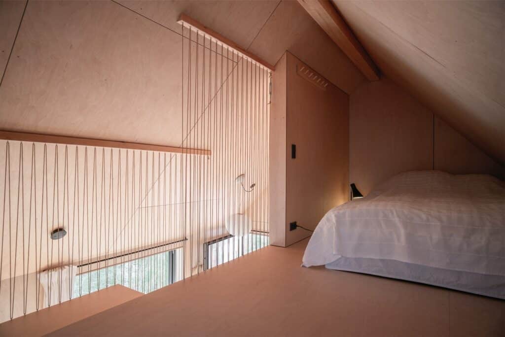 Cozy attic bedroom in Kligwood Summer House with plywood walls and a vertical string safety partition.