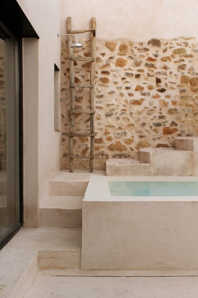 Close-up of the courtyard pool and a traditional wooden ladder against a stone and lime mortar wall.