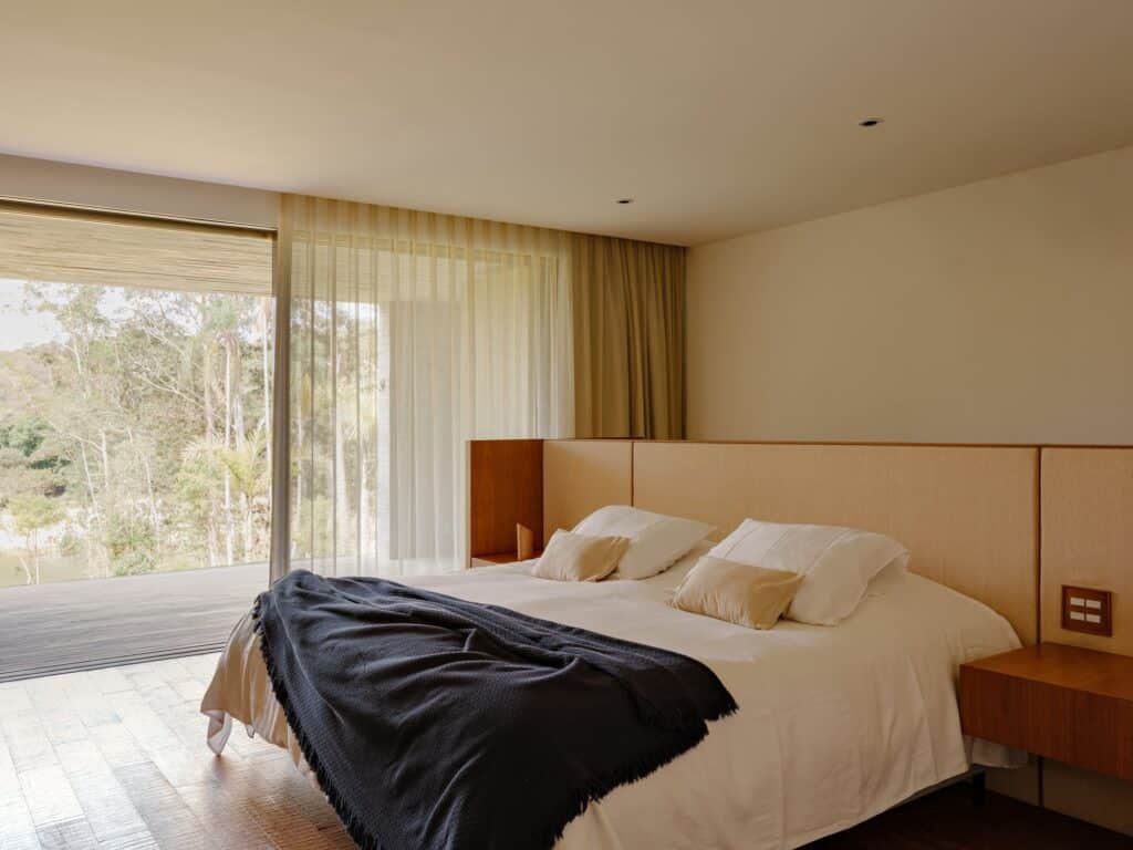 Minimalist master bedroom with wooden flooring and large sliding glass doors opening to a private view of the forest.