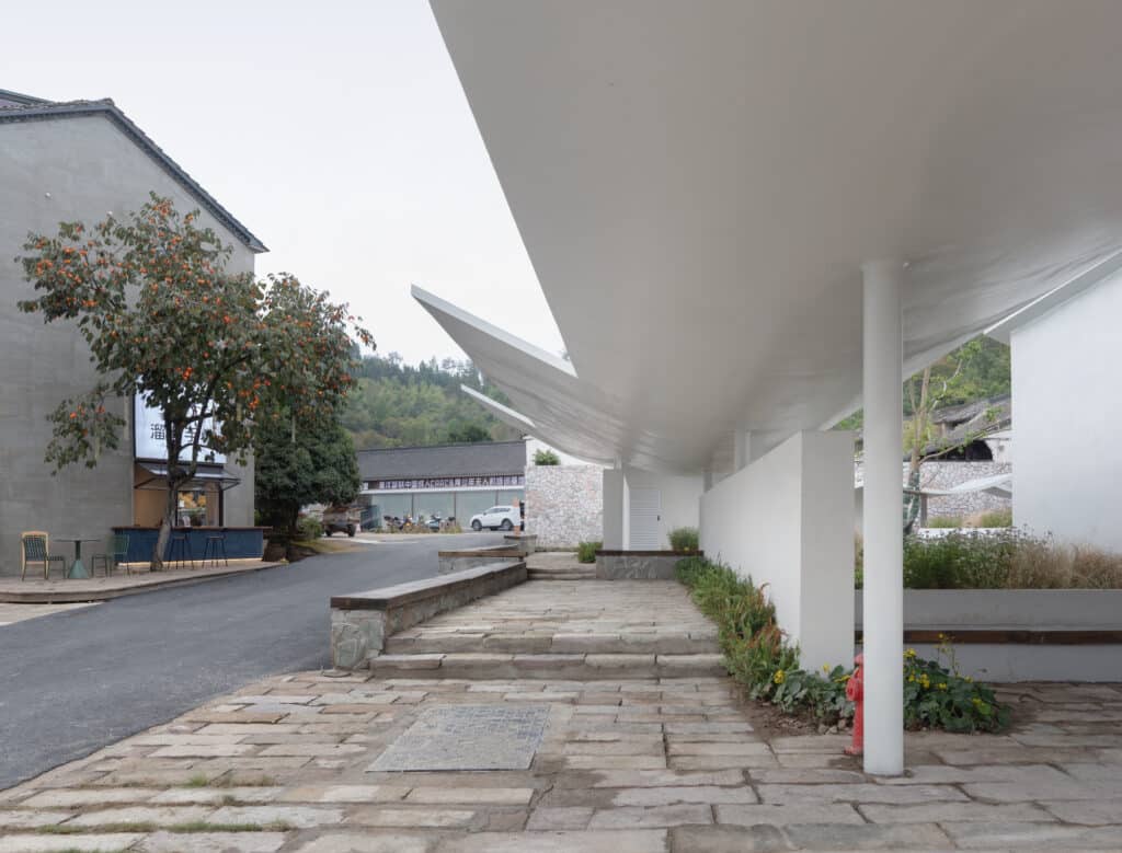 A paved pathway leading through the village with a modern curved roof structure and white walls.