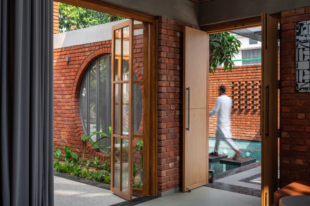 View through an open wooden door towards a water feature with stepping stones and a circular brick window detail.