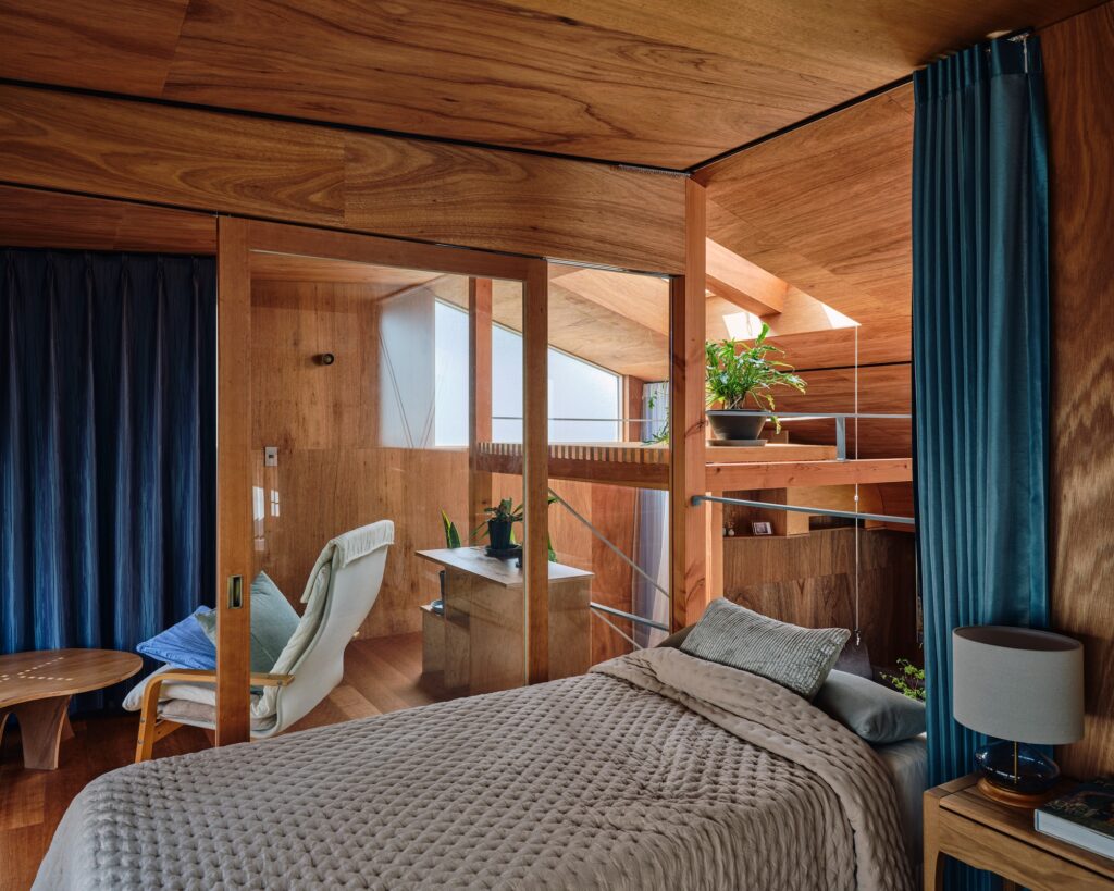 Cozy bedroom with wooden walls, a grey quilted bedspread, and a skylight providing natural illumination.