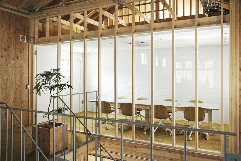 A glass-walled meeting room inside the Uchida Shoten office, framed by exposed wooden studs and a sloped ceiling.