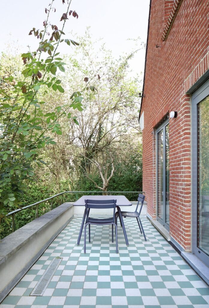 Outdoor terrace with green and white checkered tiles and a modern dining set against a red brick facade in Brussels.