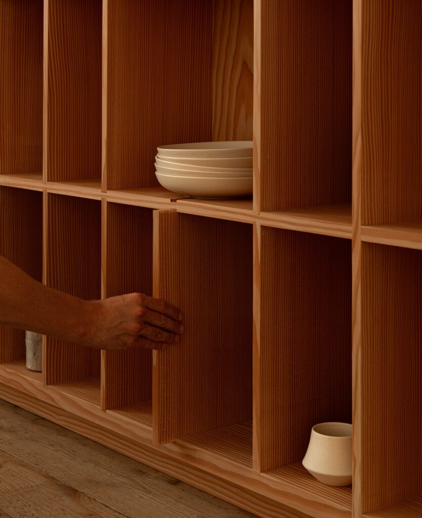 A close-up detail of a hand opening a vertical grain wooden cabinet door, showing the fine texture of the wood.