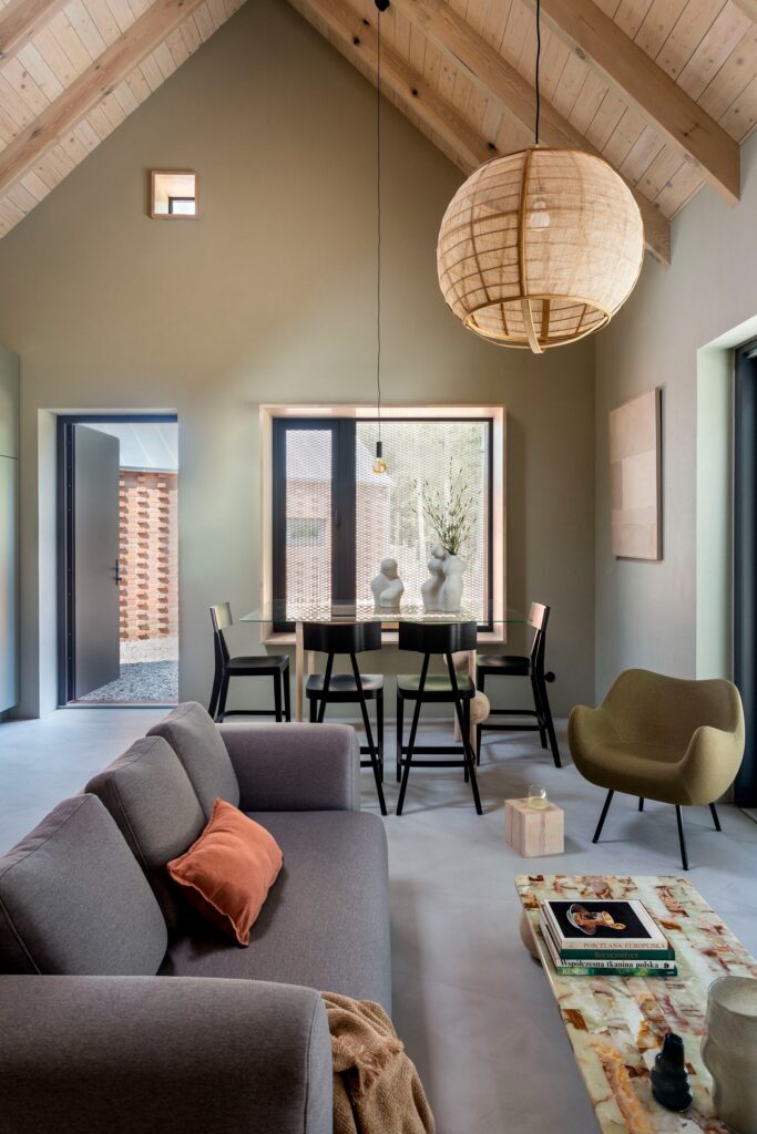 Modern interior living room of Dom Las with high vaulted ceilings, large woven pendant light, and minimalist furniture overlooking the forest.