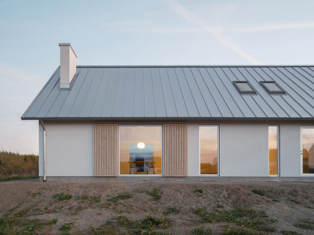 Close-up of a large window in Rorum House with a view into the warm lit dining room from the exterior.