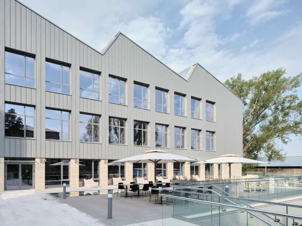 Exterior view of Narkhoz Business School showing the distinctive sawtooth roofline, gray metal cladding, and an outdoor terrace with seating.