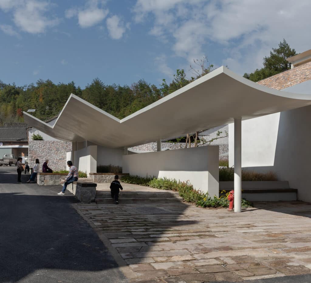 People walking up stone steps under a dynamic V-shaped roof toward a village square at Qingyi Lodge.