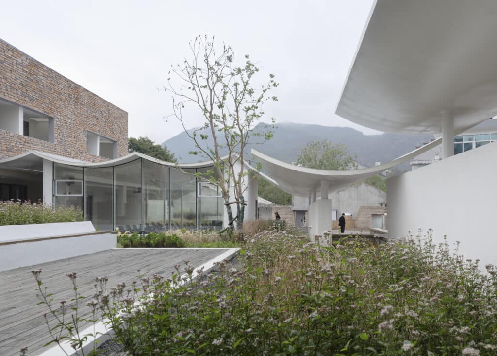 Internal courtyard of Qingyi Lodge featuring a wooden deck, glass facades, and mountain views in the distance.
