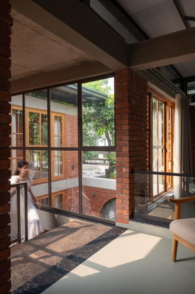 Interior view from the upper floor looking across a double-height space towards large windows and brick pillars.