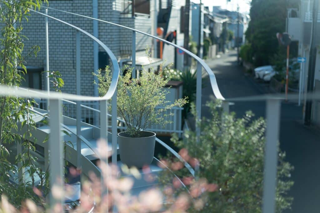 Close-up of a grey potted plant on a steel balcony with a soft-focus background of a typical Tokyo residential street.