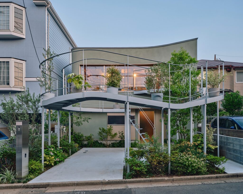 Full street-side elevation of the Tokyo house and office at twilight, showing the illuminated interior and the sculptural garden.