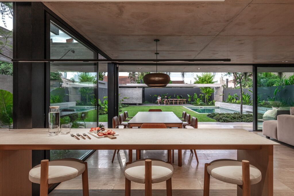 Dining area in Casa Machado viewed from the kitchen, looking out towards the garden and swimming pool across a minimalist dining table.