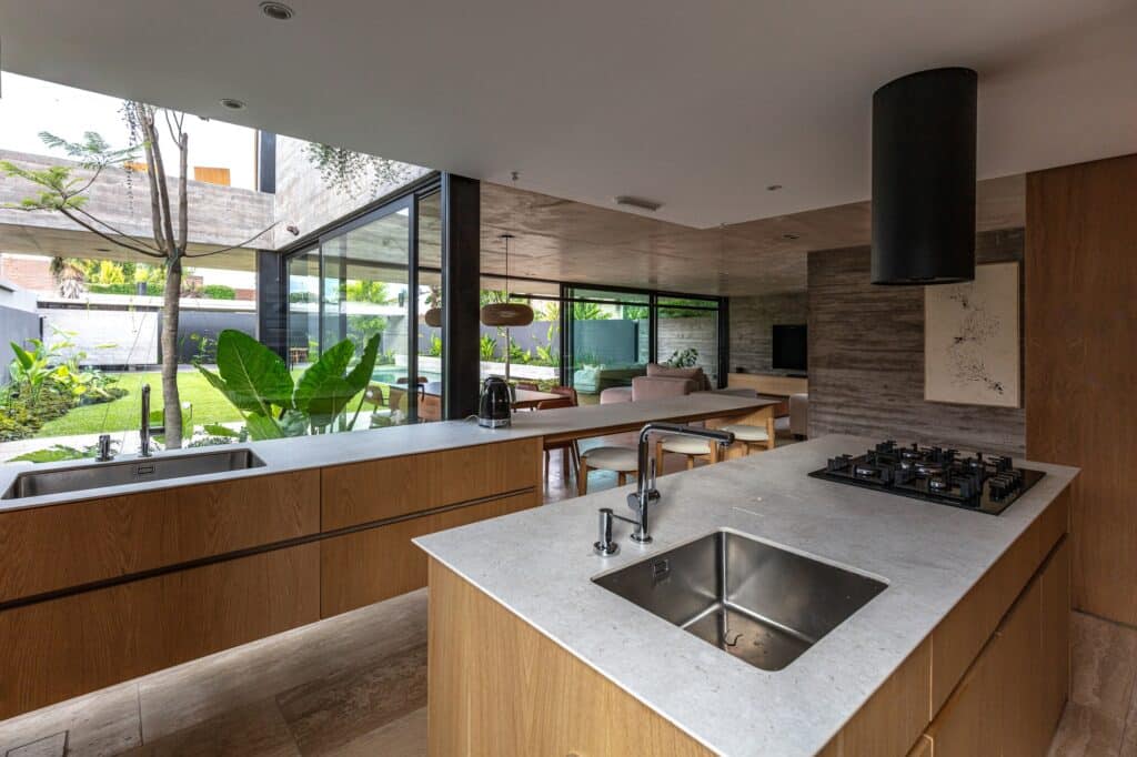 Minimalist kitchen island in Casa Machado with wooden cabinets and a view of the internal garden through large glass windows.
