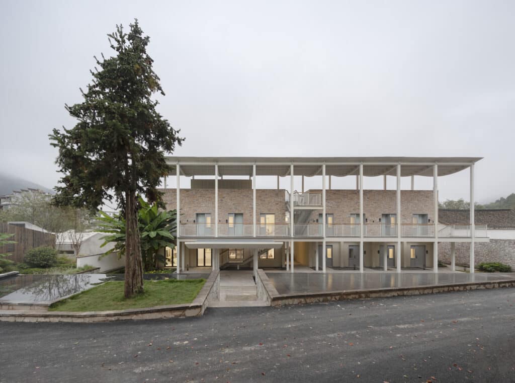 Front facade of Qingyi Lodge with a tall preserved pine tree acting as a natural landmark at the entrance.