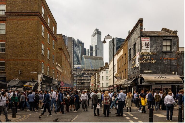 London streetscape with crowds and mixed old and new architecture, used to illustrate the A Place to Belong design competition for the London Festival of Architecture 2026.