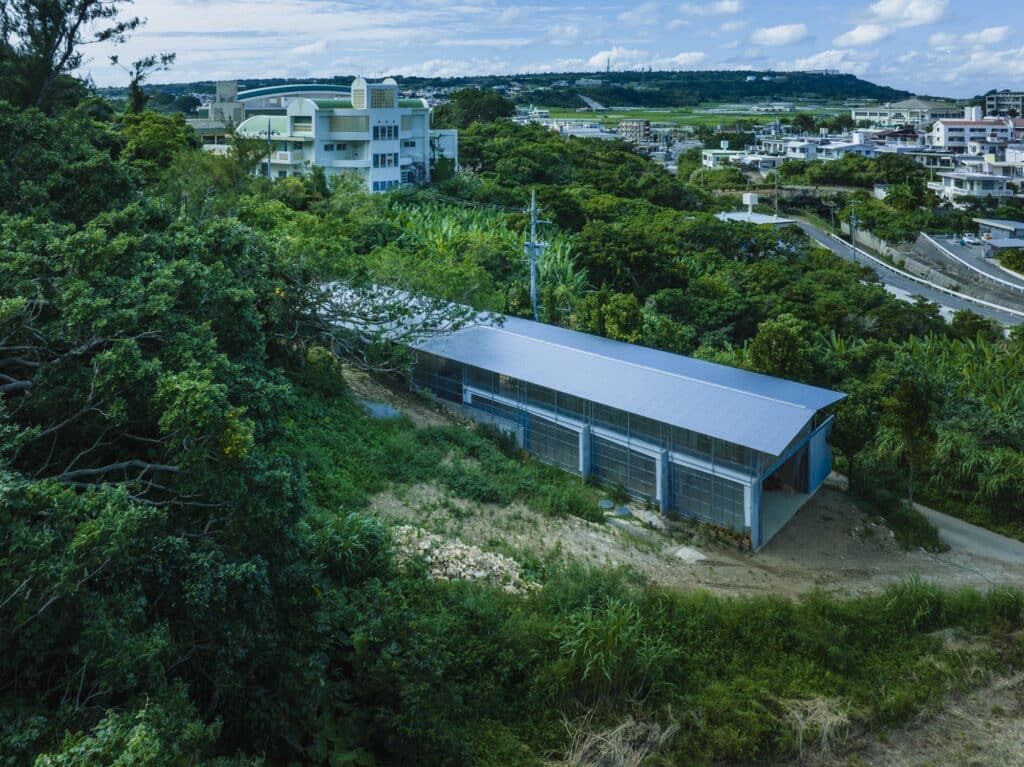 Aerial view of the long, narrow building situated on a forest edge in rural Okinawa.
