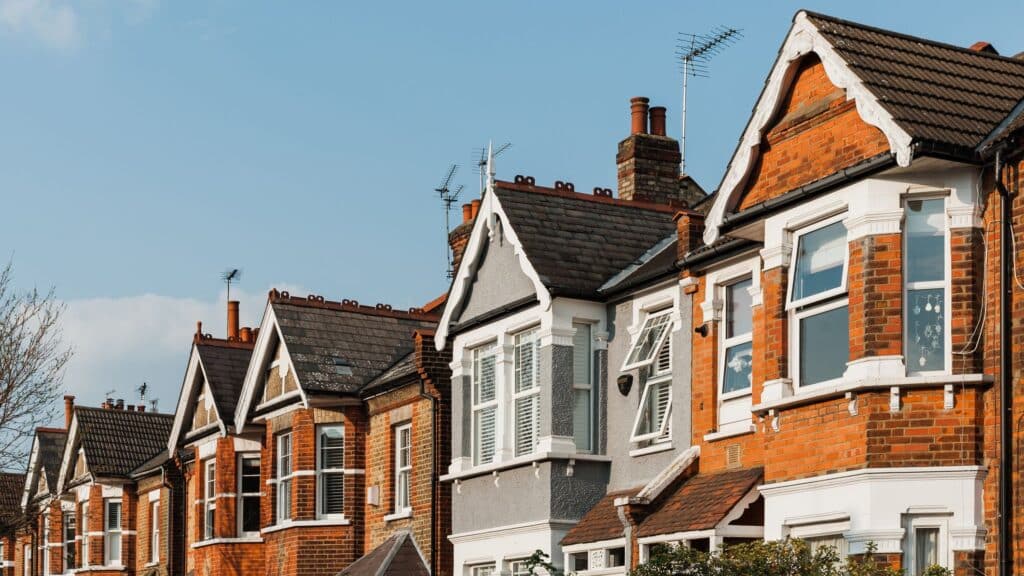 A row of colorful, multi-story brick terraced houses with gabled roofs, bay windows, and white trim under a clear blue sky.