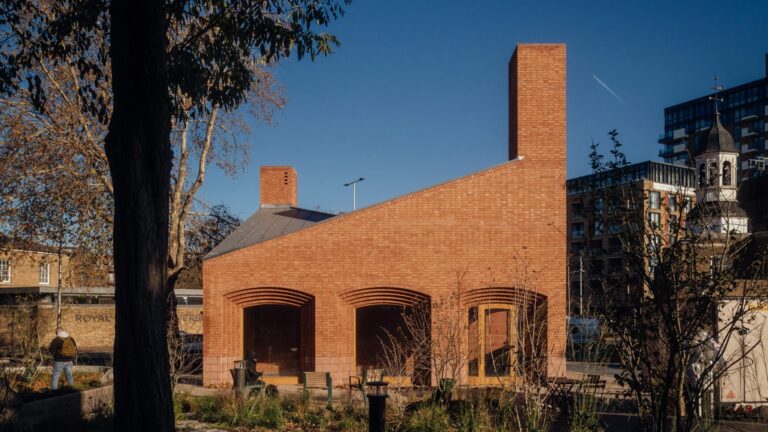 A modern red brick building with a striking asymmetrical sloped roof and a tall integrated chimney under a clear blue sky.