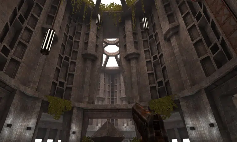 A first-person perspective in a video game showing a massive, circular concrete hall with brutalist architecture, hanging vines, and a futuristic weapon held in the foreground.