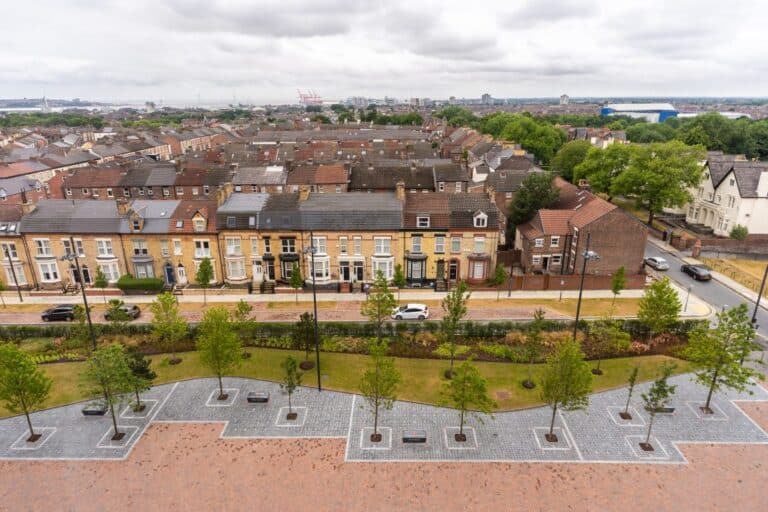 Aerial view of terraced housing in Liverpool, showcasing traditional brick facades, pitched roofs, and newly landscaped public green space with tree-lined pathways — illustrating urban regeneration efforts ahead of the 63,000-home development plan.