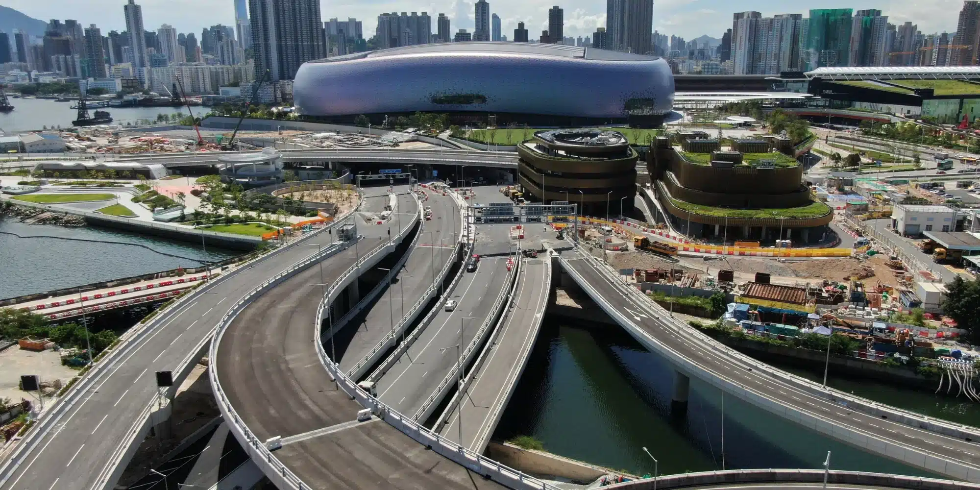 Aerial view of the Central Kowloon Bypass in Hong Kong, showing curved elevated roadways intersecting near West Kowloon Station and the M+ Museum.
