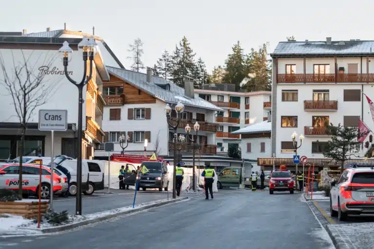 Police and emergency personnel at the Crans-Montana ski resort street following a New Year’s Eve fire incident, with snow-dusted alpine buildings and cordoned-off area under investigation.