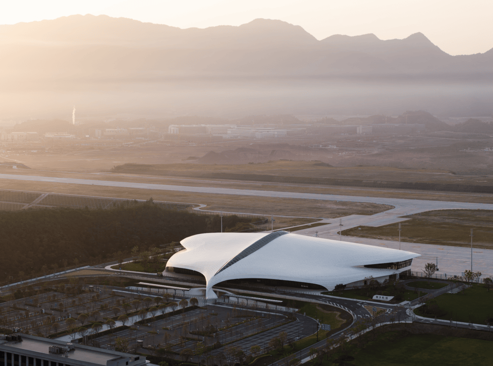 Aerial view of the organic white terminal building at Lishui Airport glowing under soft sunset light against a misty mountain backdrop.