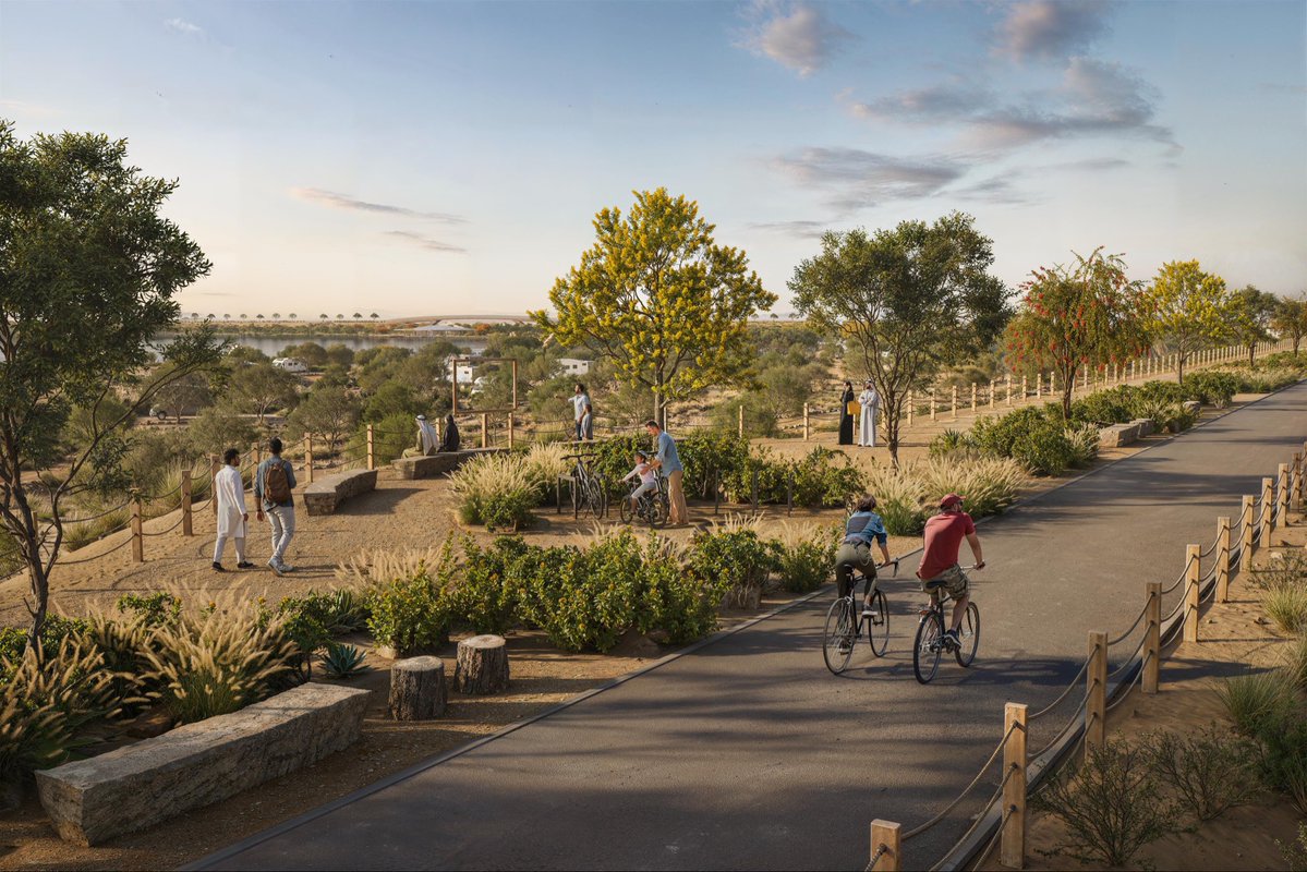 An aerial view of the expansive Desert Oasis Project, showcasing the central blue lake surrounded by lush green landscaping and modern architectural structures set against the desert sand.