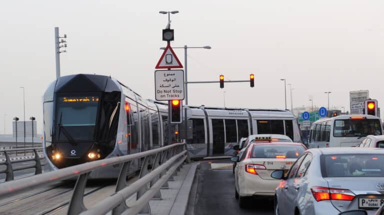 Existing Dubai tram navigating busy intersection with private cars, illustrating the traffic congestion the new Trackless Tram system aims to solve.