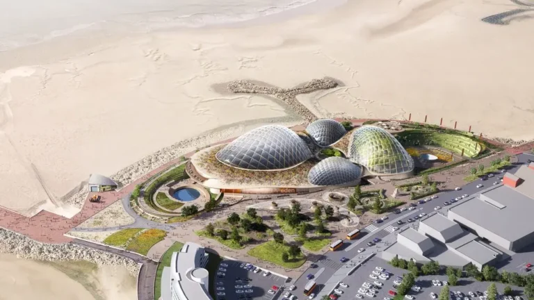 Aerial view of Eden Morecambe showing the arrangement of glass biomes on the sandy Lancashire coastline near existing urban infrastructure.