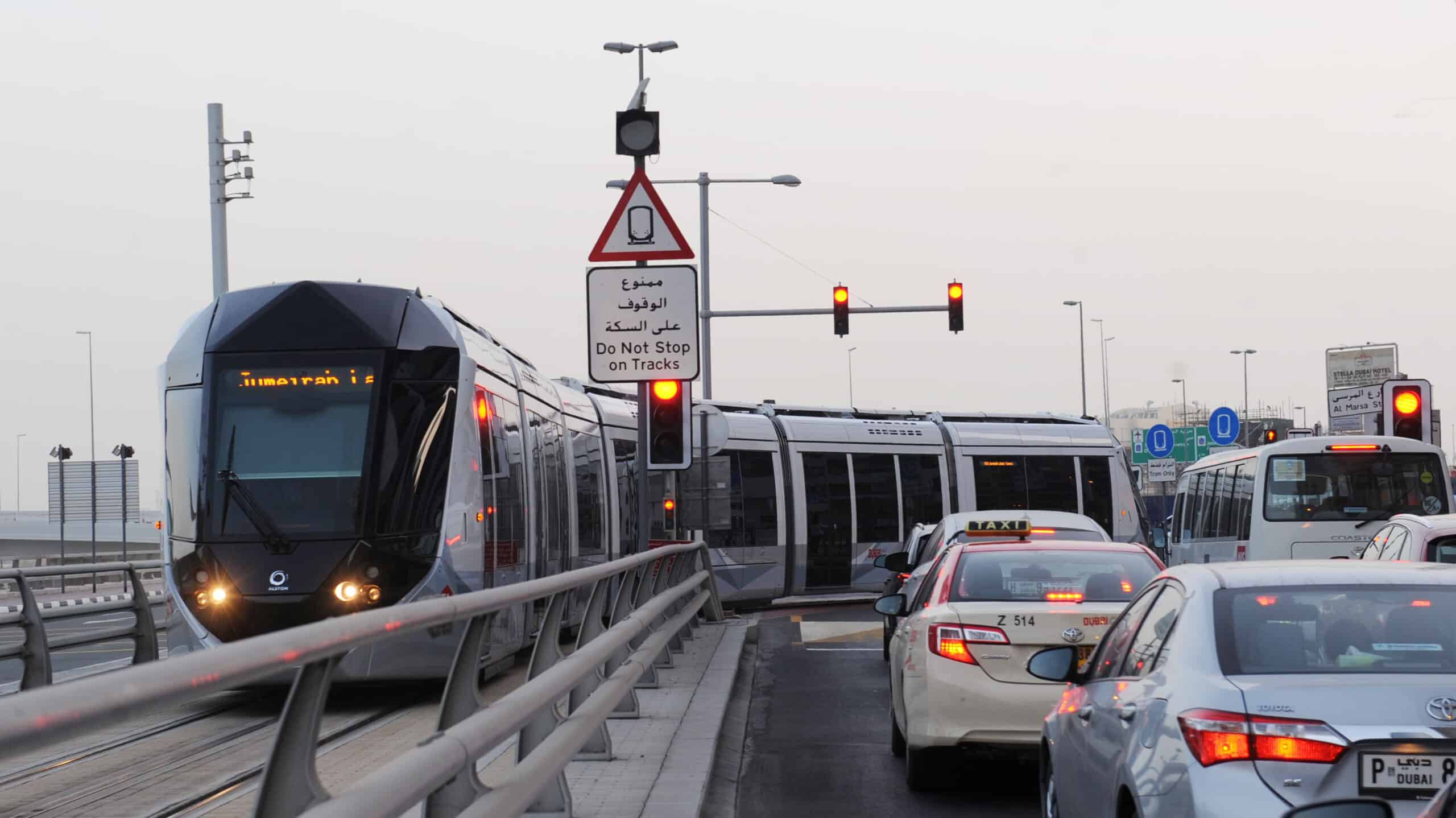 Existing Dubai tram navigating busy intersection with private cars, illustrating the traffic congestion the new Trackless Tram system aims to solve.