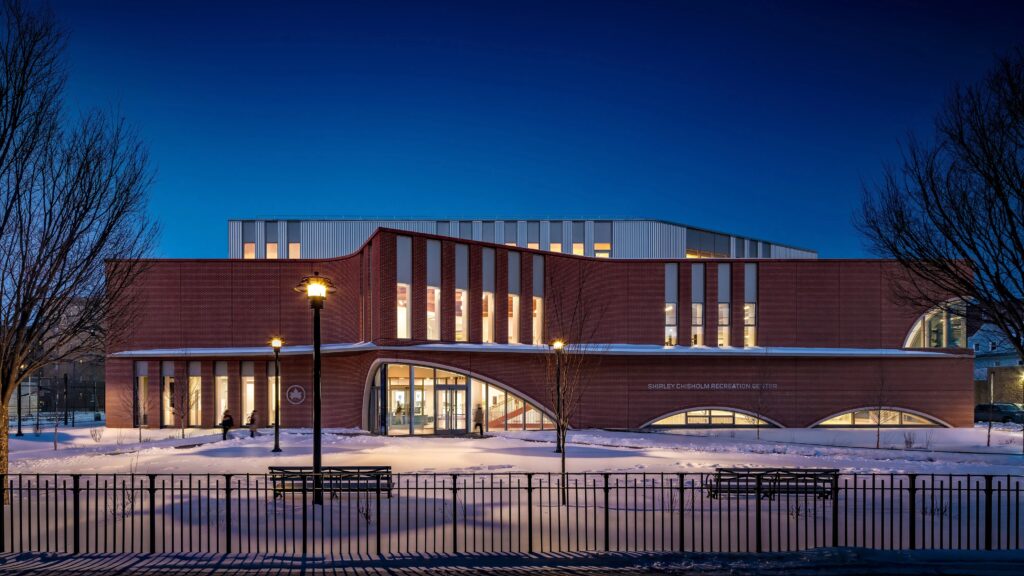 The striking curved brick facade of the new Brooklyn Community Recreation Center, with large arched windows reflecting the daylight.