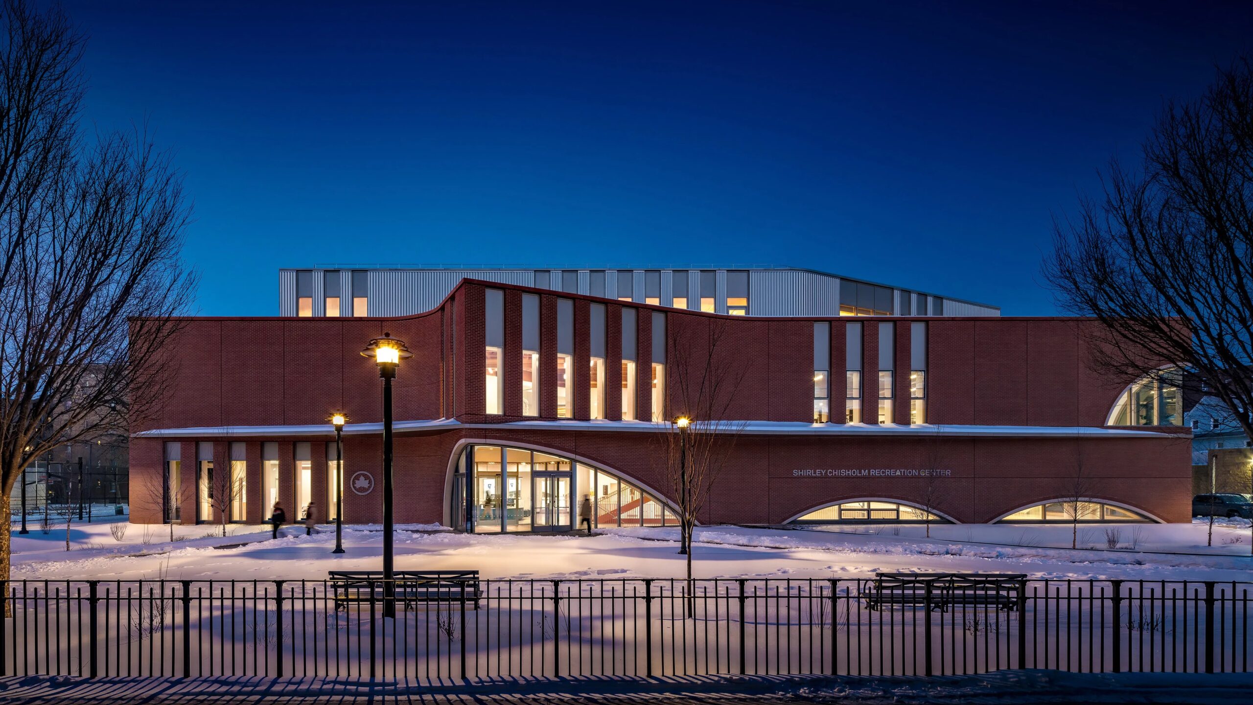 The striking curved brick facade of the new Brooklyn Community Recreation Center, with large arched windows reflecting the daylight.