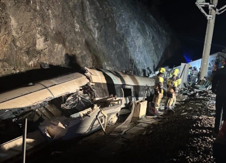 Emergency responders inspecting the twisted wreckage of the carriage against a rock face during the Spain Train Disaster.