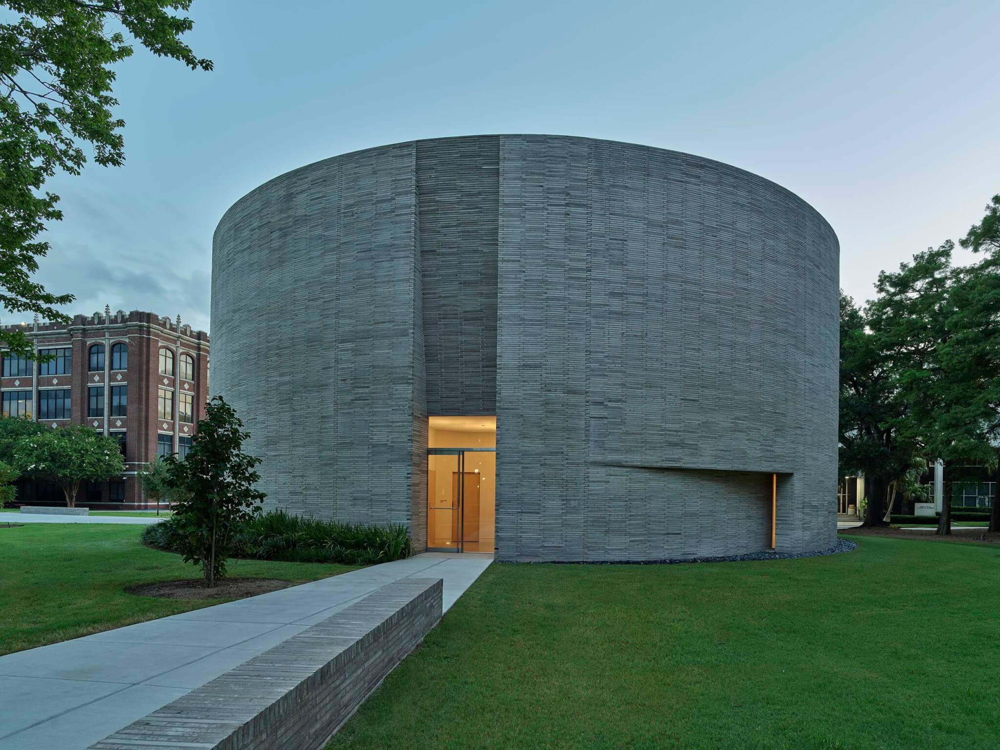 A monolithic Circular Chapel clad in grey-white brick features a minimalist glass entrance and curved facade.