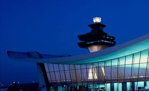 Night view of the Eero Saarinen-designed terminal at Washington Dulles International Airport featuring a curved concrete roof and glass facade, a classic example of modernist transportation infrastructure design.