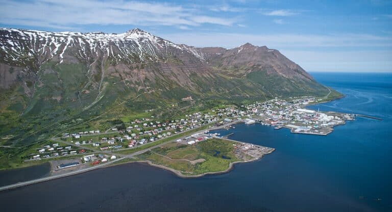 Aerial view of Siglufj&ouml;r&eth;ur coastal town nestled between steep mountains and the fjord, the northern terminus for the new Iceland tunnel project designed to bypass hazardous mountain routes.