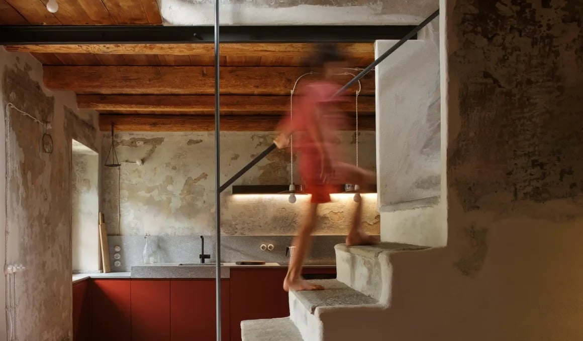 The exterior of a historic stone house after a complete alpine home restoration, showing the traditional stone slab roof and surrounding greenery.