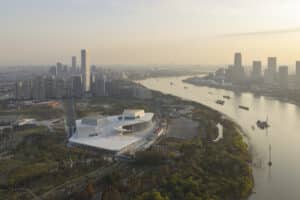 Aerial view of the Shanghai Grand Opera House featuring a white radial roof design situated along the Huangpu River at sunset.